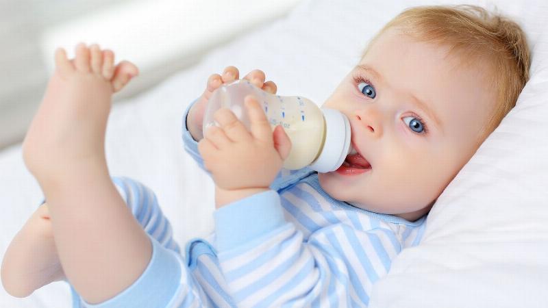 Hình ảnh em bé 7 đến 12 tháng tuổi vừa ăn dặm vừa uống sữa theo bảng ml sữa chuẩn cho bé